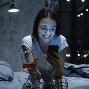 Bettbeziehung: Junge Frau schaut auf ihr Handy und lacht